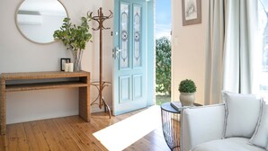 A room with a wooden floor, a wicker console table, a coat rack, a blue door, a white chair, a small table with a potted plant, and a framed picture on the wall. - Bluebird Cottage – cheerful and cosy home, short distance to Bowral (Bowral)