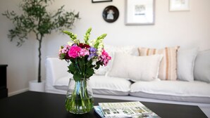 A living room with a glass vase of flowers on a black table, a white sofa with striped pillows, and a magazine on the table. - Bluebird Cottage – cheerful and cosy home, short distance to Bowral (Bowral)