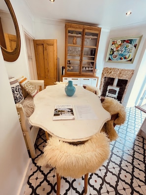 A dining area with a round table, a blue vase, and a magazine. There is a wooden cabinet with glass doors in the background.