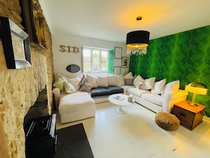 A living room with a white sofa, a black ottoman, a round coffee table, and a green accent wall.