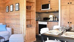 A cozy wooden interior with a dining area, kitchen, and a sofa with a blue pillow. - Cozy studio near slopes - 4 guests (Méribel)