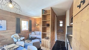 A cozy cabin interior with a dining area, a sofa, and a built-in wooden shelf unit. - Cozy studio near slopes - 4 guests (Méribel)
