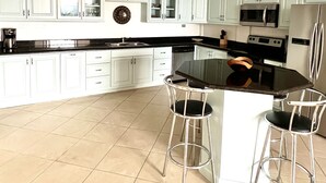 A kitchen with light blue cabinets, a central island with stools, a ceiling fan, and modern appliances. - Seaside Serenity; 2b/2b with Panoramic Terrace (Playas Del Coco)