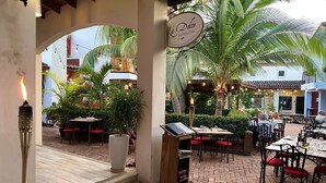 An outdoor dining area with tables and chairs, a sign for 'La Dolce Vita International Restaurant & Pizzeria', and a staircase leading to an upper level. - Charming condo with a rooftop, across beach (Playas Del Coco)