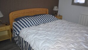 A neatly made bed with a striped pillow and a white duvet, a wooden headboard, a bedside table with a lamp, and a framed picture on the wall. - Charming 2-room cabin in central Font-Romeu, parking included (Font-Romeu-Odeillo-Via)