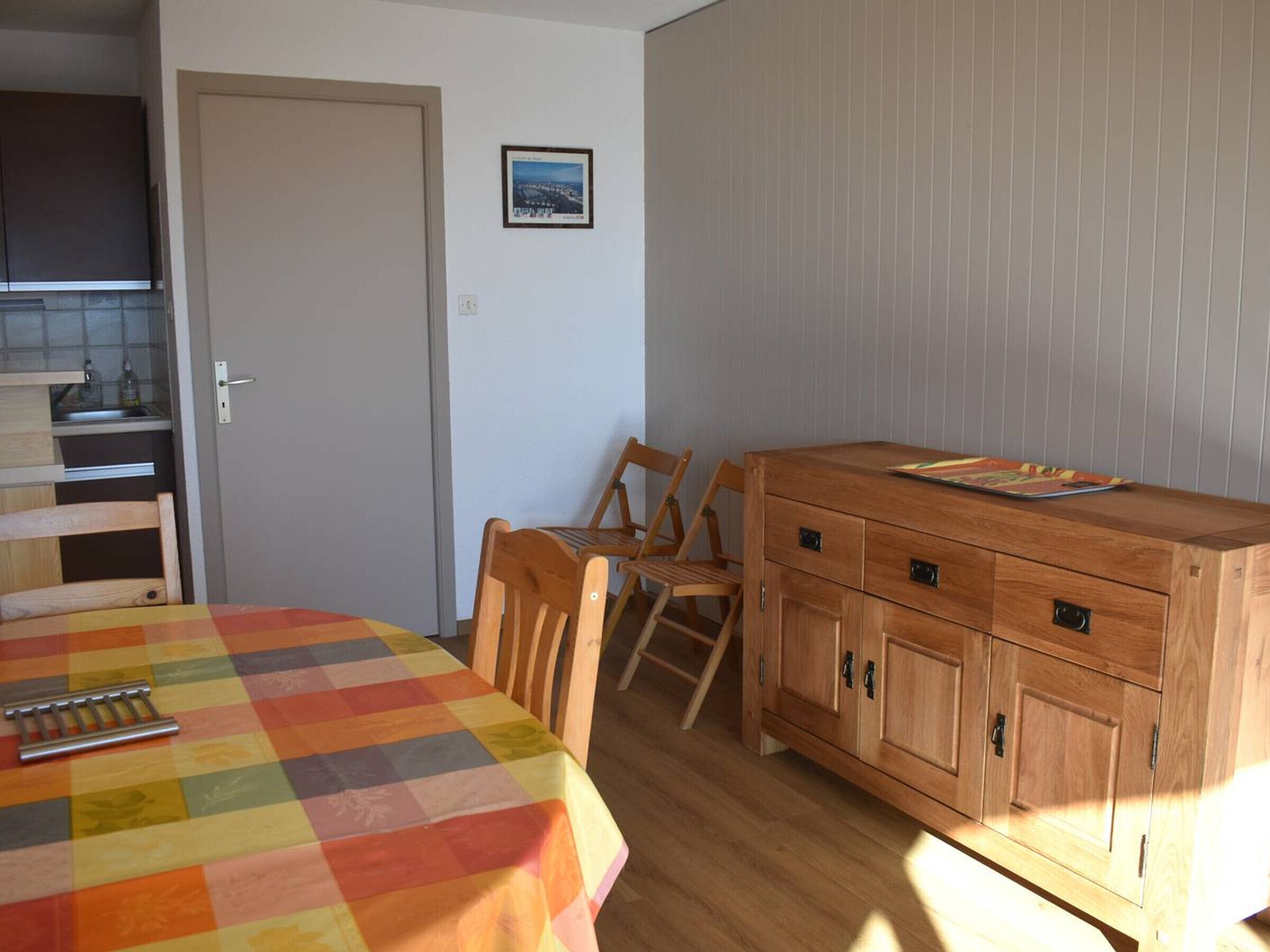 Ein Zimmer mit einem Holzkasten, einem Tisch mit bunter Tischdecke und einem Stuhl.
