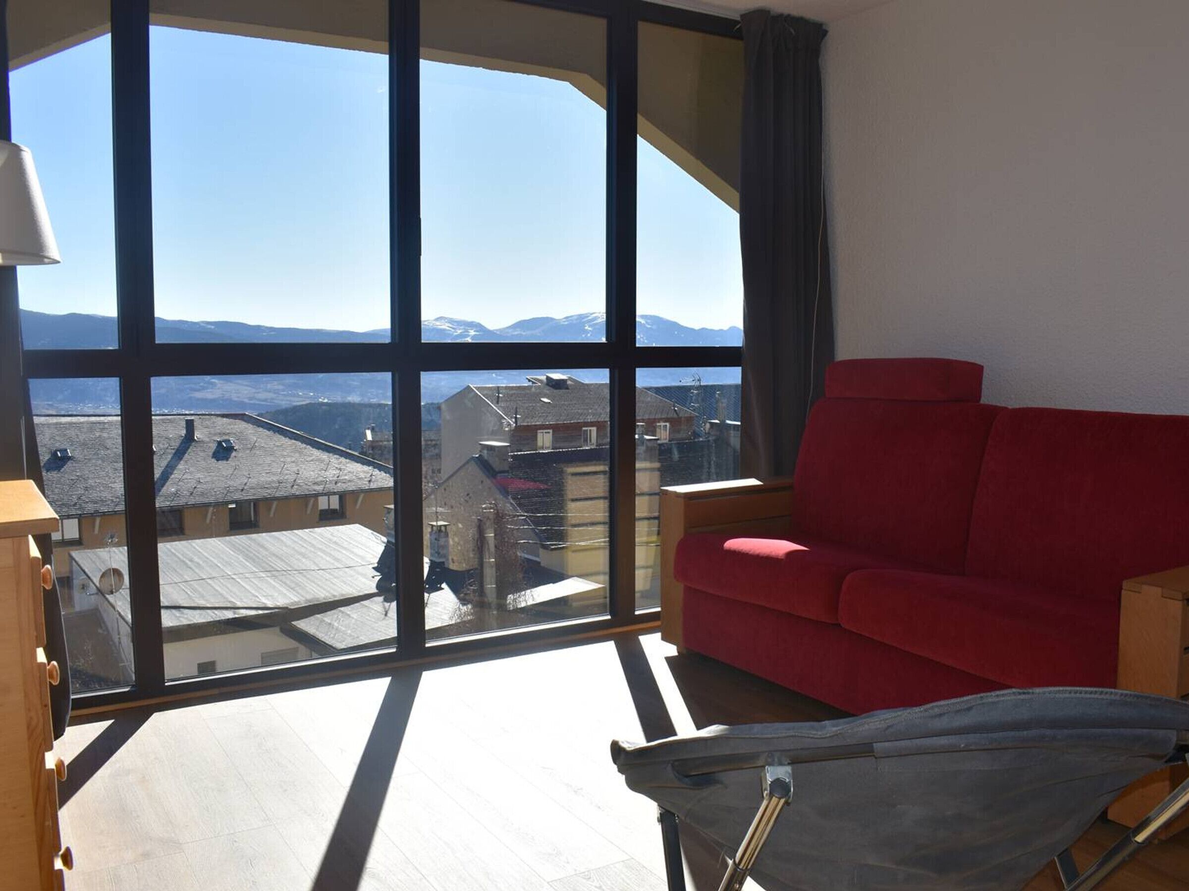 A spacious balcony with a red sofa and a chair, overlooking a mountainous landscape.