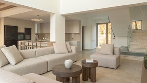 A spacious living area with a large sectional sofa, a coffee table, and a dining area with chairs. - Casa Beleza Villa, a Mythical Retreat (Perama)