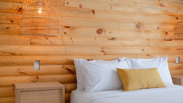 A wooden log cabin room with a bed, white pillows, a yellow pillow, and a woven nightstand. - #10 - Studio/Plateau/St-Denis/SelfCheck-In/AC/TV (Montréal)