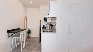 Una cuina compacta amb armaris blancs, forn integrat, rentamics d'acer inoxidable i una petita zona de bar amb tamborets blancs.