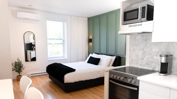 A modern room with a bed, a dining area, a kitchen with a stove and microwave, and a window with curtains. - #11 - Studio/Plateau/St-Denis/SelfCheck-In/AC/TV (Montréal)