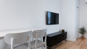 A modern room with a white desk, two white chairs, a black console table, and a mounted flat-screen TV. - #11 - Studio/Plateau/St-Denis/SelfCheck-In/AC/TV (Montréal)