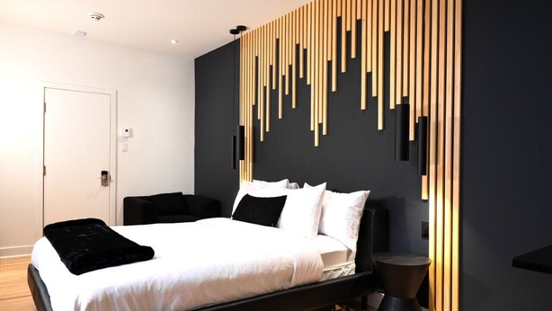 A modern bedroom with a bed, a black bedside table, a wooden wall panel, and a door. - #6 - Studio/Plateau/St-Denis/SelfCheck-In/AC/TV (Montréal)