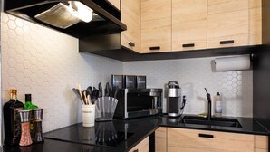 A modern kitchen with a black countertop, wooden cabinets, a microwave, a coffee maker, and a utensil holder. - #6 - Studio/Plateau/St-Denis/SelfCheck-In/AC/TV (Montréal)