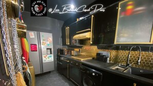 A modern kitchen with black cabinets, a stainless steel sink, and a microwave. There is a refrigerator with a small window and a neon sign on the wall. - Stay & Play at Lovebehindcloseddoors (Plymouth)