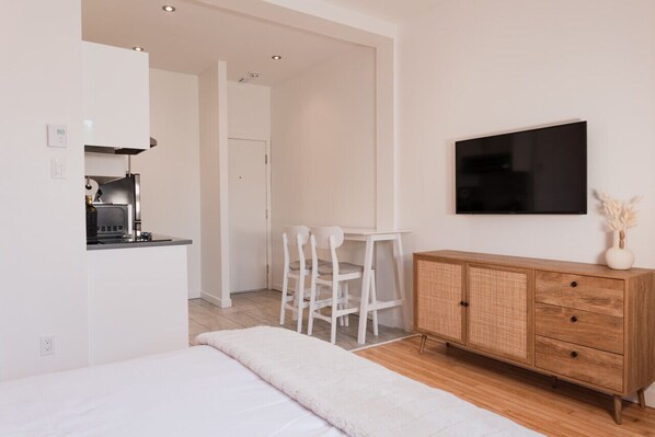 Une chambre moderne équipée d’un lit, d’une télévision, d’une commode en bois et d’un coin cuisine.