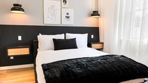 A modern bedroom with a bed, black and white bedding, two bedside lamps, a wall-mounted speaker, and abstract art.