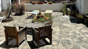 Eine Terrasse mit Steinboden, Holzmöbeln und Topfpflanzen.