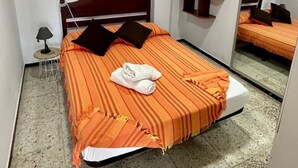 Ein Schlafzimmer mit Bett, Deckenventilator, Nachttisch, Lampe, Spiegel und einem Bild an der Wand.