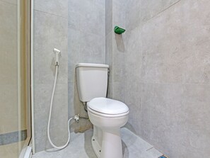 A bathroom with a toilet, a shower hose, and a green soap dispenser.