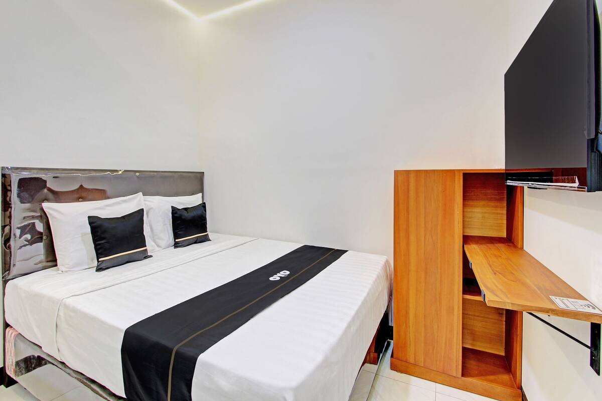 A modern hotel room with a neatly made bed, a wooden nightstand, and a flat-screen TV mounted on the wall.