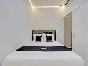 A small, neatly made bed with a black and white bedspread and two pillows, a white door, and a white wall.