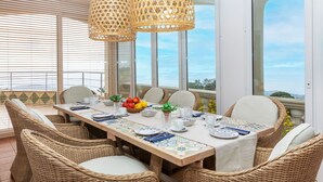 Un coin repas avec des meubles en osier, une longue table et deux lampes en rotin suspendues.