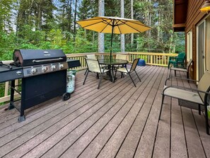 Eine Holzterrasse mit Grill, Tisch und Stühlen sowie einem Sonnenschirm.