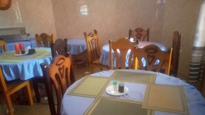 Un comedor con mesas redondas cubiertas con manteles azules, sillas de madera y una mesa central con posavasos.