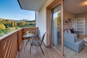 A balcony with a table and chairs, a sliding glass door leading to a living area with a sofa and cushions.