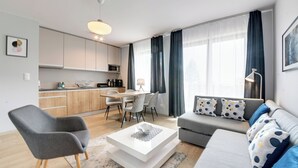 A modern living room with a sofa, armchair, and coffee table. There is a kitchen area with cabinets and a microwave. - RentPlanet - Apartamenty Bawaria (Szklarska Poreba)