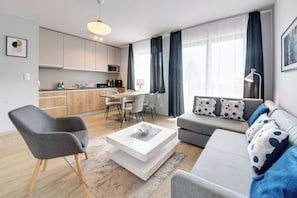 A modern living room with a sofa, armchair, and coffee table. There is a kitchen area with cabinets and a microwave. - RentPlanet - Apartamenty Bawaria (Szklarska Poreba)