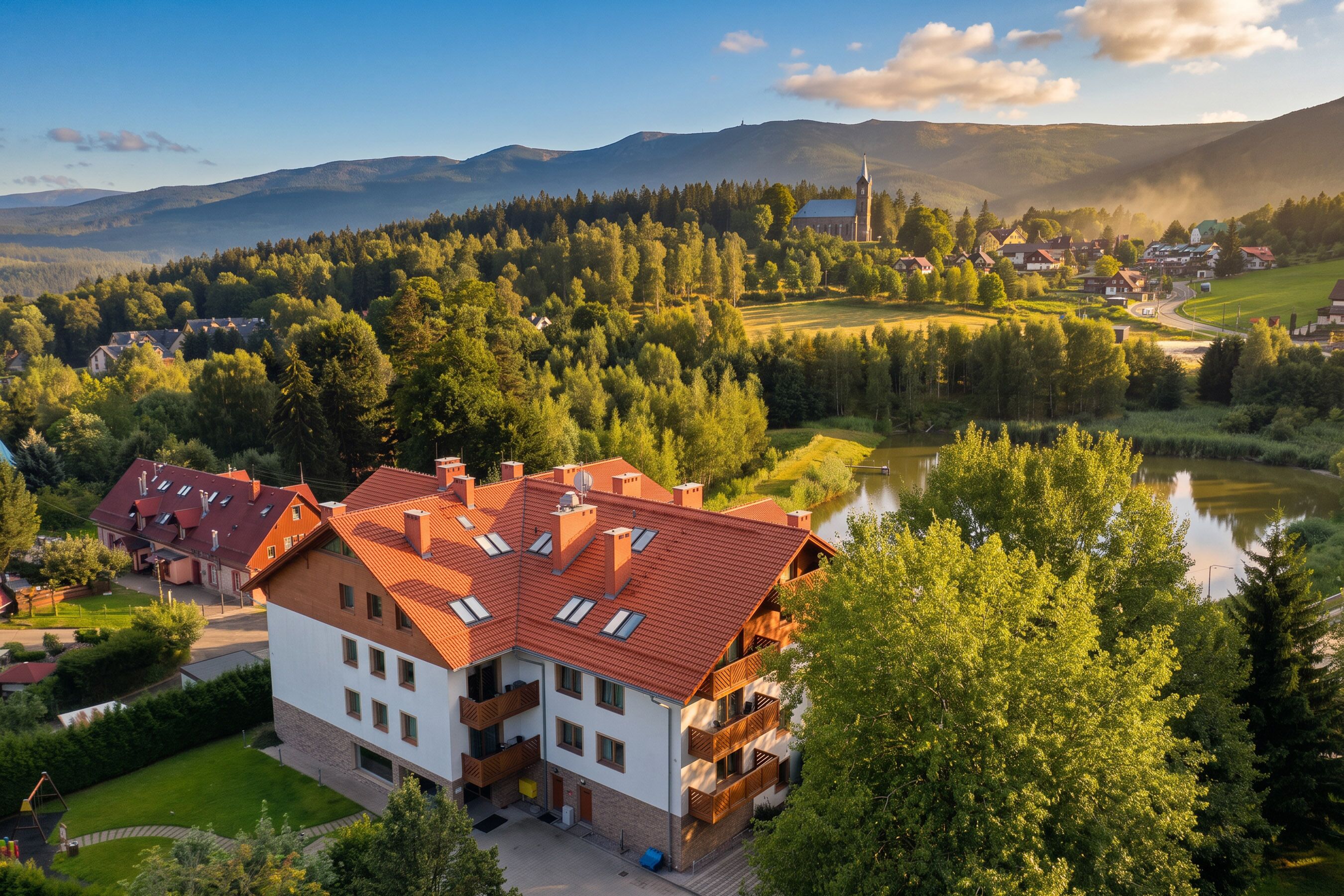A multi-story building with a red-tiled roof, surrounded by lush greenery and a river.
