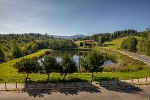 A serene lakeside view with a paved walkway, trees, and a distant building. - RentPlanet - Apartamenty Bawaria (Szklarska Poreba)