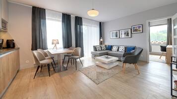 En moderne stue med spiseplads, en grå sofa med mønstrede puder, en kaffemaskine og et stort vindue med gardiner.