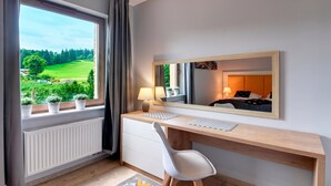 A modern hotel room with a wooden desk, a white chair, a large window with a view of a green landscape, and a mirror reflecting the room. - RentPlanet - Apartamenty Bawaria (Szklarska Poreba)