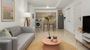 A modern living room with a grey sofa, a round coffee table with books and a vase, a TV, and a kitchen in the background. - Azure 32 (Cape Town)