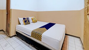 A single bed with a white mattress, blue and yellow patterned pillows, and a blue and yellow blanket. The room has beige walls and a tiled floor. - SPOT ON 92983 Hotel Ayu (Semarang)