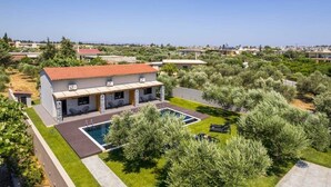 Een modern huis met een zwembad, omringd door groen en andere huizen.