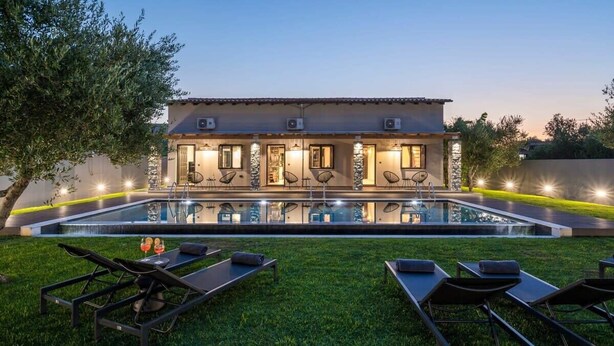Een moderne villa met een zwembad, terras en een goed verlichte gevel.