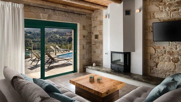 Un salon chaleureux avec un mur en pierre, une cheminée et une vue sur une piscine et des montagnes.