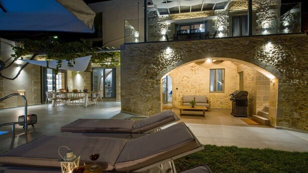An outdoor seating area with lounge chairs and a table with drinks, a stone archway, and a barbecue grill. - Casa di Grimpili (Kolimvari)