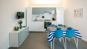 A modern kitchen with white cabinets, a built-in oven, and a dining area with a striped tablecloth and blue chairs.