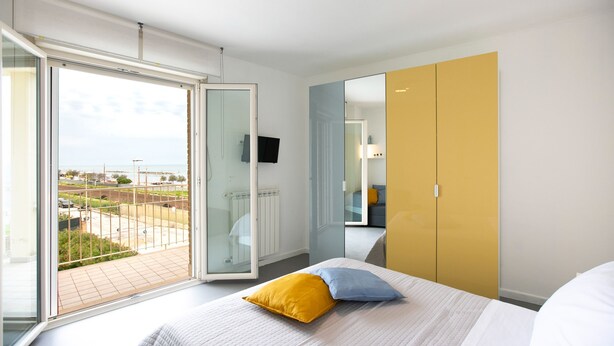 A modern hotel room with a large bed, a sliding glass door to a balcony, and a yellow wardrobe.