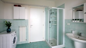 A bathroom with a glass-enclosed shower, a sink, a washing machine, and a radiator.