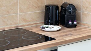 Et køkken med en sort induktionskogeplade, en kaffemaskine og en tallerken med kaffekapsler.
