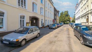 En smal gade fyldt med parkerede biler og bygninger i klassisk arkitektur.