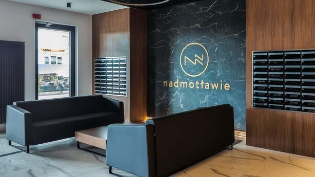 A modern reception area with a marble wall, a logo, and a seating area with a sofa and a bench. - Elegant Apartment | Balcony with View of the Motława River, Gymnasium (Gdansk)