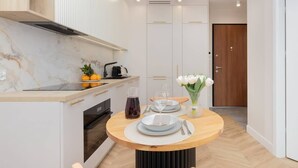 A modern kitchen with white cabinetry, a built-in oven, and a round wooden table set for dining. - Elegant Apartment | Balcony with View of the Motława River, Gymnasium (Gdansk)