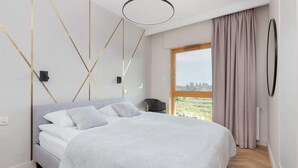 A modern bedroom with a large bed, a city view through the window, and a minimalist design. - Elegant Apartment | Balcony with View of the Motława River, Gymnasium (Gdansk)